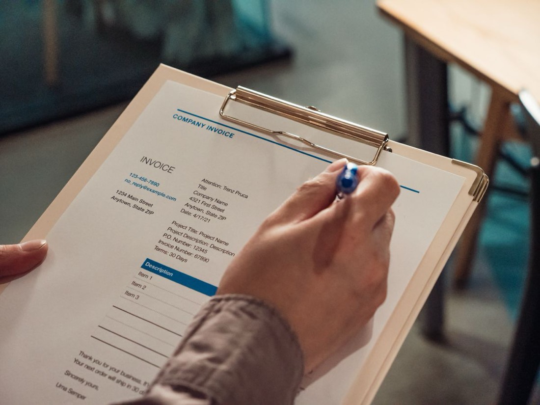 A supplier invoice on a clipboard being reviewed by hand