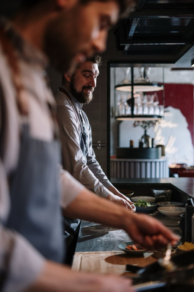 Two cooks plating dishes at a restaurant pass